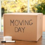 Cardboard box with words MOVING DAY and packaging items on wooden table