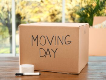 Cardboard box with words MOVING DAY and packaging items on wooden table