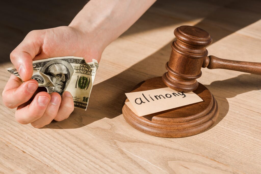 cropped view of man holding crumpled dollar banknote near gavel and paper with alimony lettering on