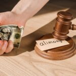 cropped view of man holding crumpled dollar banknote near gavel and paper with alimony lettering on
