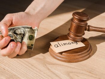 cropped view of man holding crumpled dollar banknote near gavel and paper with alimony lettering on