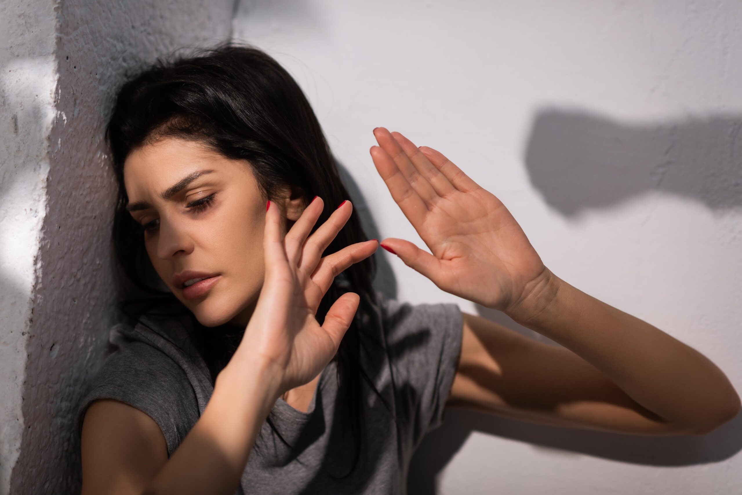 selective focus of depressed woman with bruise on face gesturing near shadow, domestic violence