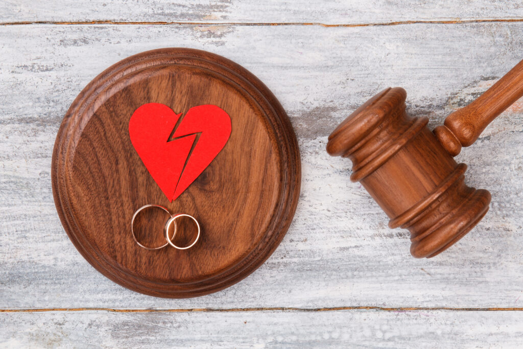 Top view broken heart and gavel. Pair of wedding rings. White wood background.